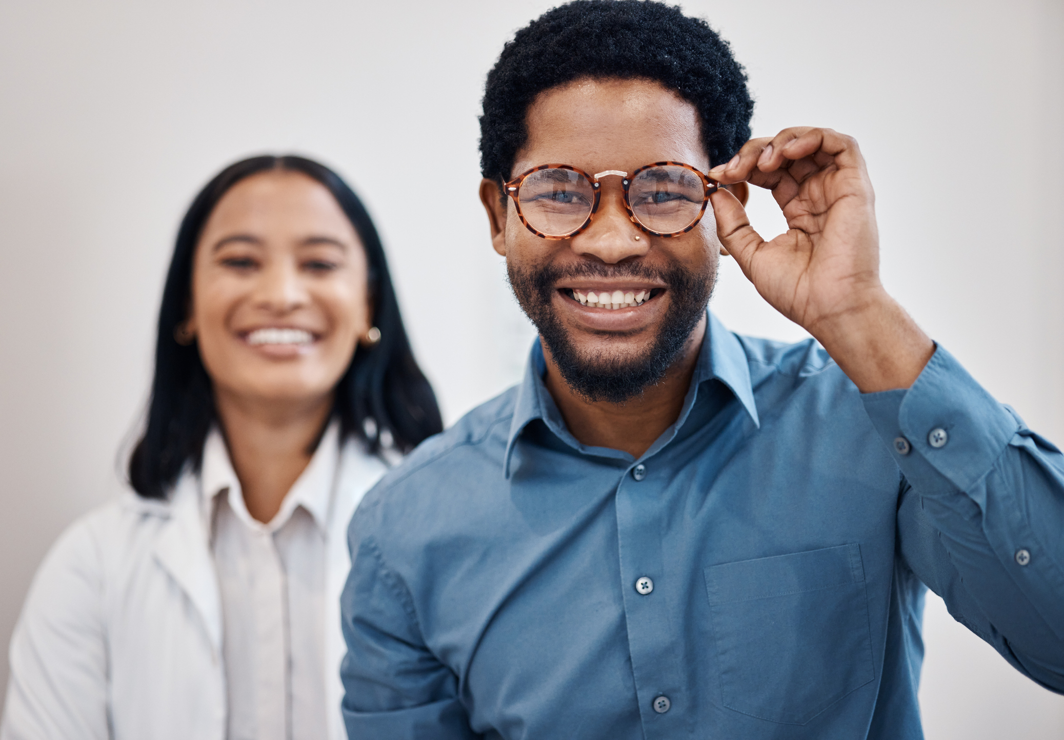 A young man admires his new pair of prescription eyeglasses as his optometrist looks on.