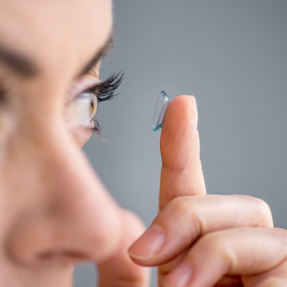 A woman places a prescription contact in her eye.